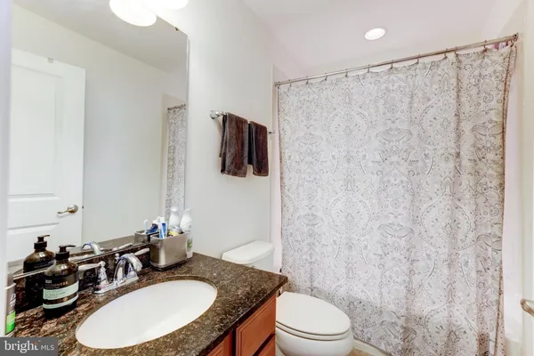 a bathroom with a granite countertop sink toilet a mirror and shower curtain