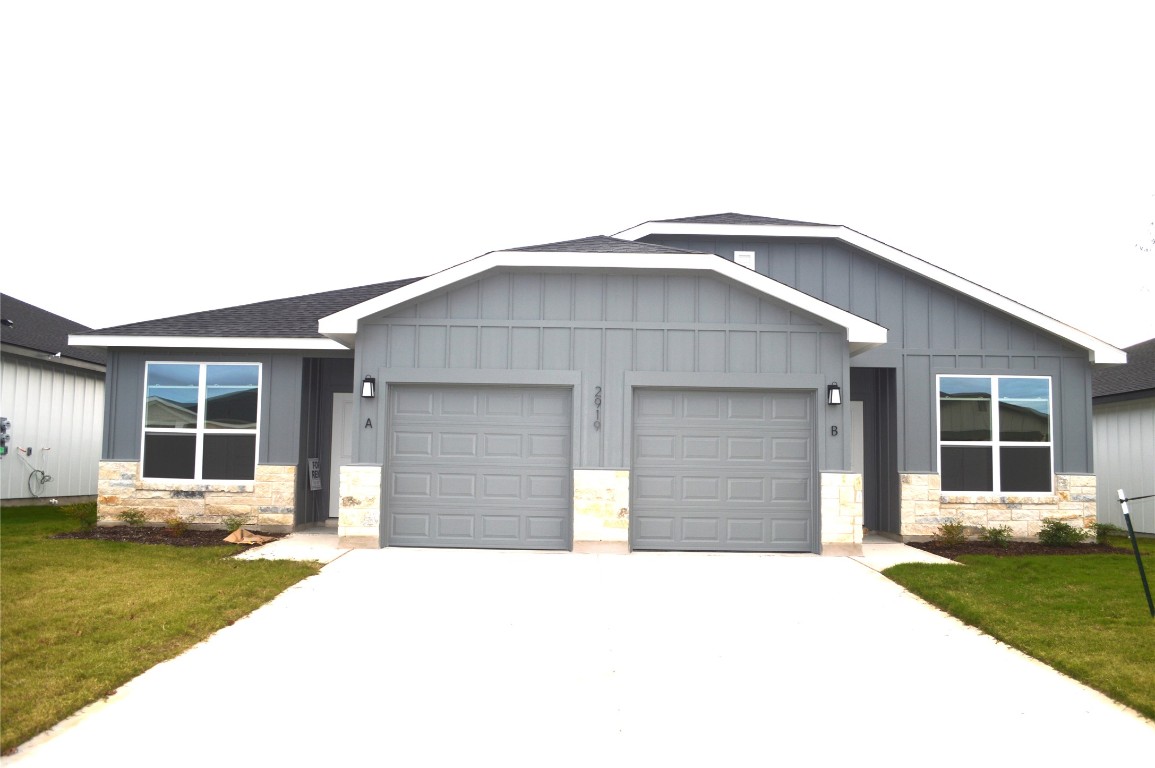 Ranch-style house featuring stone siding, board and batten siding, a front yard, and concrete driveway