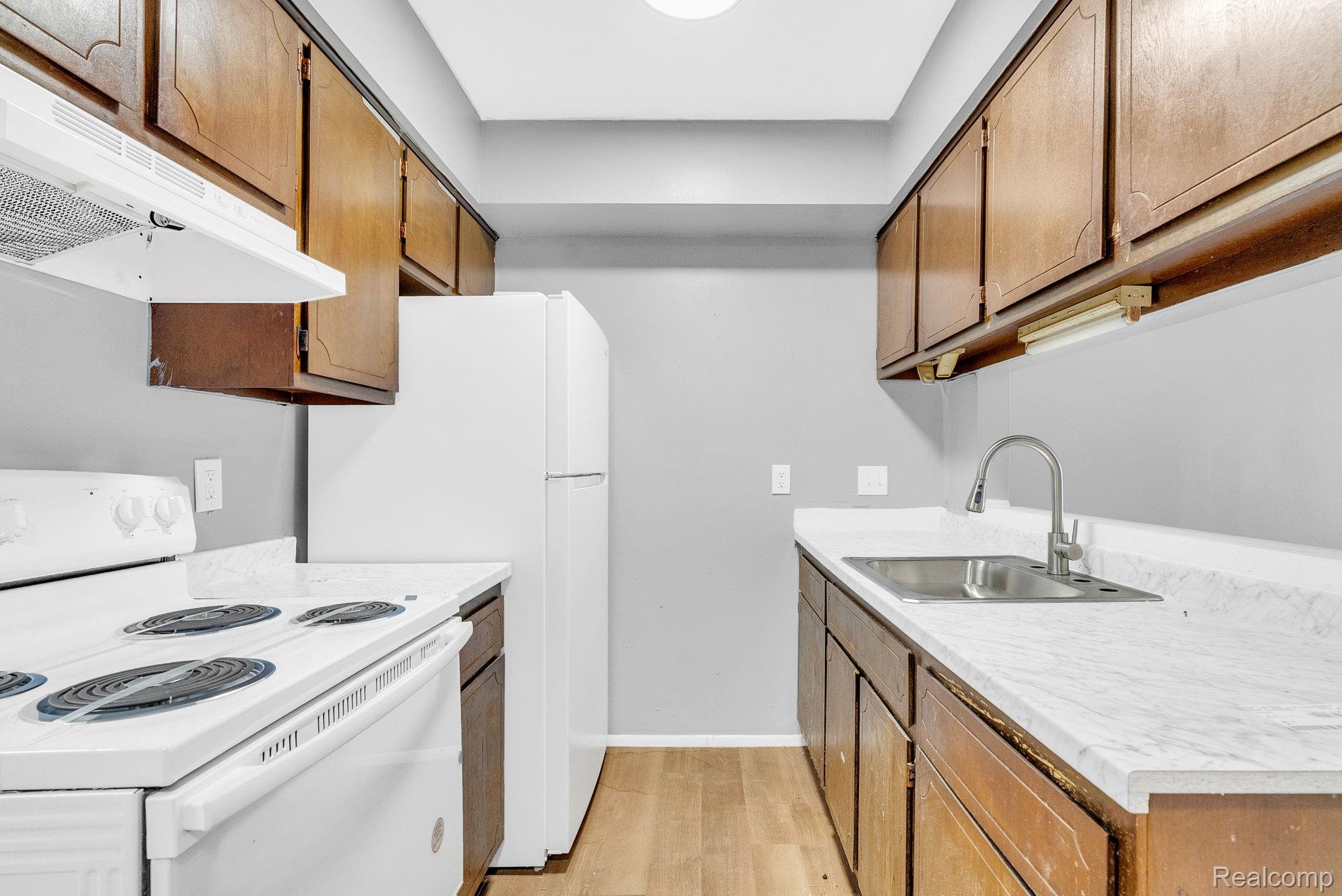 4535 Cadieux Road, Unit 42 / 210 Detroit, MI 48224 - Photo 9 of 16 Kitchen featuring white appliances, under cabinet range hood, light countertops, light wood finished floors, and brown cabinets