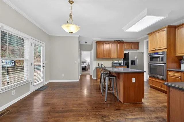 a open kitchen with stainless steel appliances granite countertop a stove top oven a sink a dining table and chairs with wooden floor