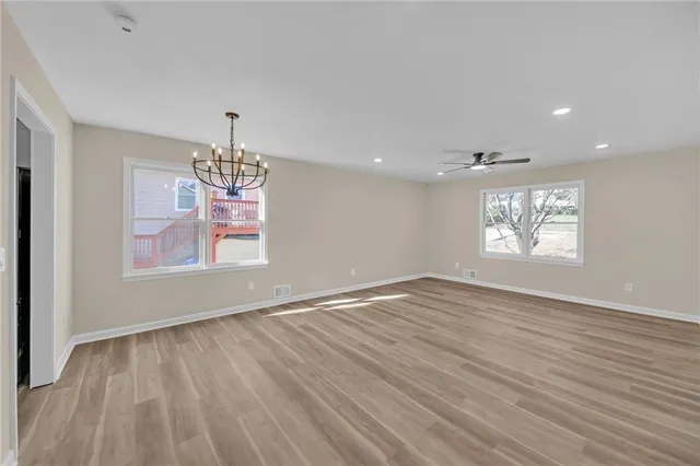 an empty room with wooden floor chandelier and windows