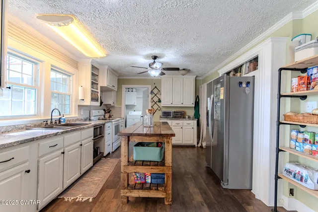 a kitchen with stainless steel appliances granite countertop a refrigerator a sink dishwasher a stove and white countertops with wooden floor