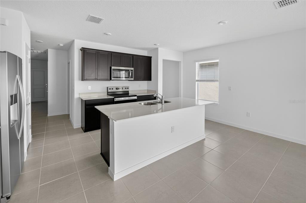 6784 Southwest 90th Loop Ocala, FL 34476 - Photo 8 of 11 a kitchen with stainless steel appliances a stove top oven a sink a refrigerator white cabinets and wooden floor