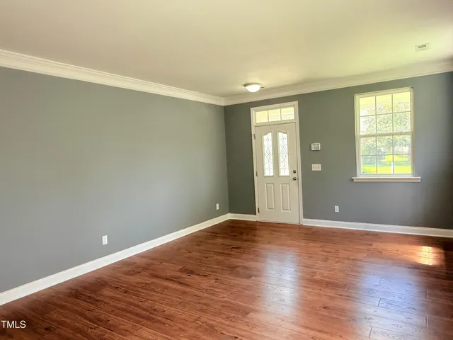 a view of an empty room with window and wooden floor