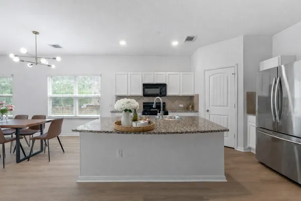 a kitchen with stainless steel appliances granite countertop a stove top oven a refrigerator a dining table and chairs with wooden floor