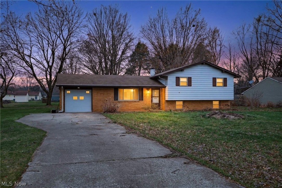 Tri-level home featuring a yard, concrete driveway, brick siding, and a garage
