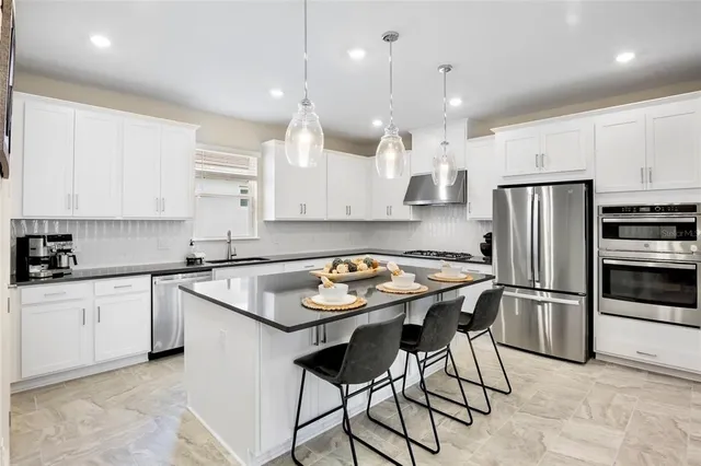 a kitchen with kitchen island a refrigerator a stove a sink and white cabinets