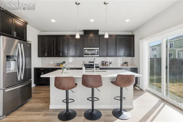 a kitchen with stainless steel appliances granite countertop a refrigerator a stove a sink and a dining table with wooden floor