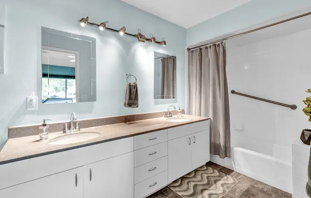 a bathroom with a double vanity sink a mirror a bathtub and shower