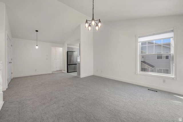 Carpeted living area with white walls, a large window, a modern chandelier, and an additional pendant light