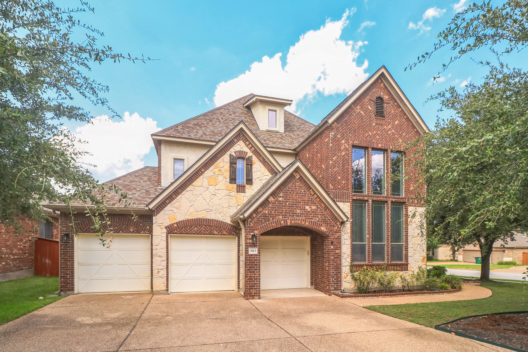 A classic brick and stone facade meets a spacious three-car garage and paved driveway.