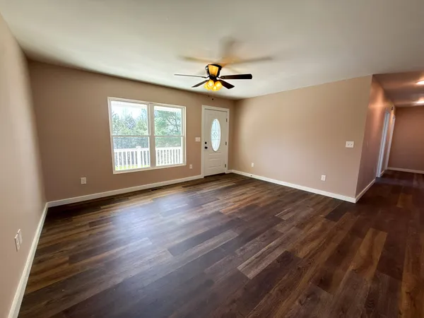 an empty room with wooden floor chandelier fan and windows