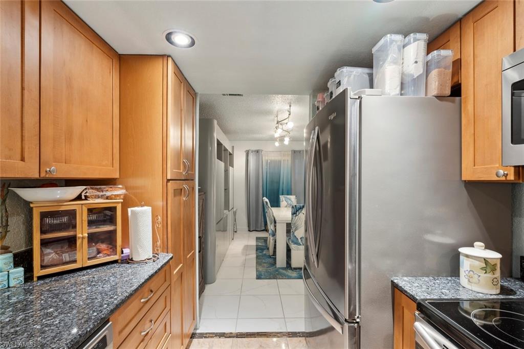 126 Harrison Road, Unit M3 Naples, FL 34112 - Photo 17 of 48 Kitchen featuring dark stone countertops, visible vents, appliances with stainless steel finishes, and brown cabinetry
