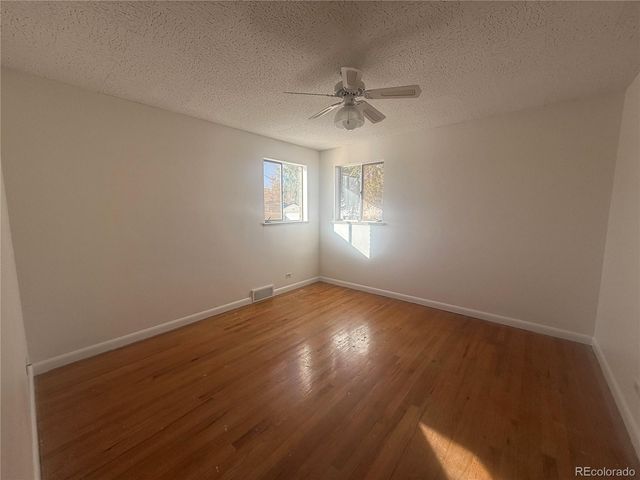 an empty room with wooden floor fan and windows