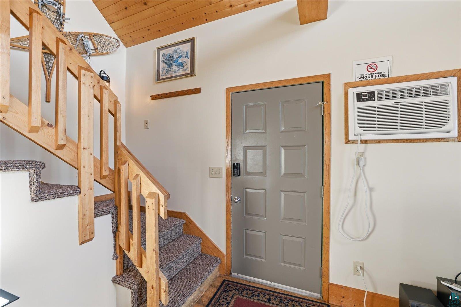6266 Giants Ridge Road Biwabik, MN 55705 - Photo 7 of 29 Entryway featuring a paneled door with wood trim, a window-mounted air conditioning unit, and a carpeted staircase with wood banisters