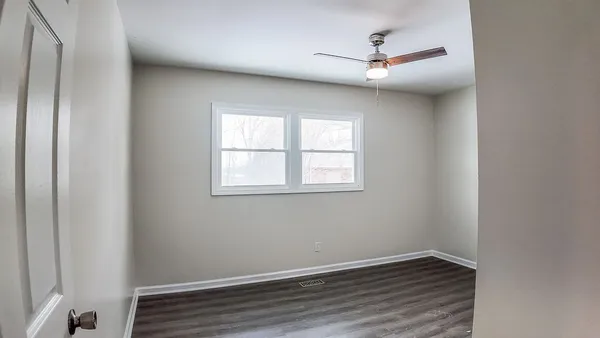 an empty room with wooden floor ceiling fan and windows