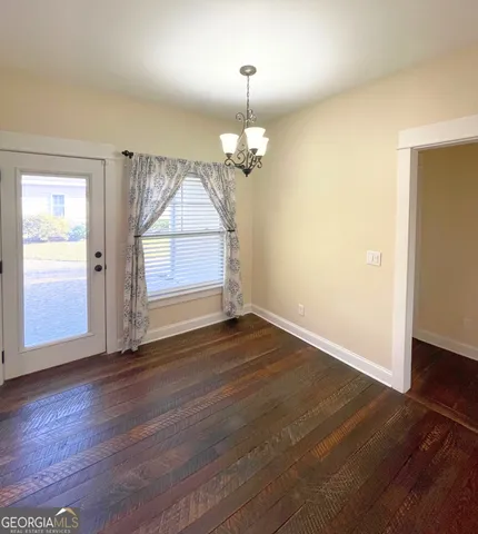an empty room with wooden floor chandelier and windows