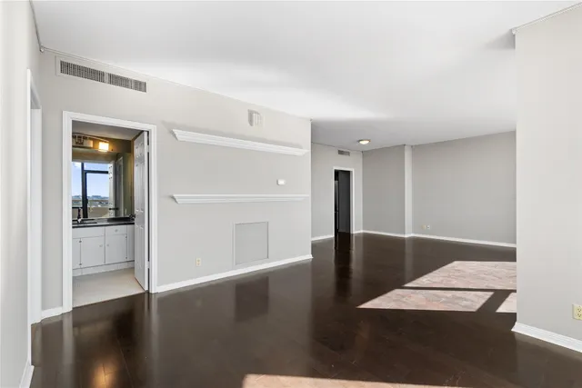 a view of an empty room with wooden floor and a kitchen