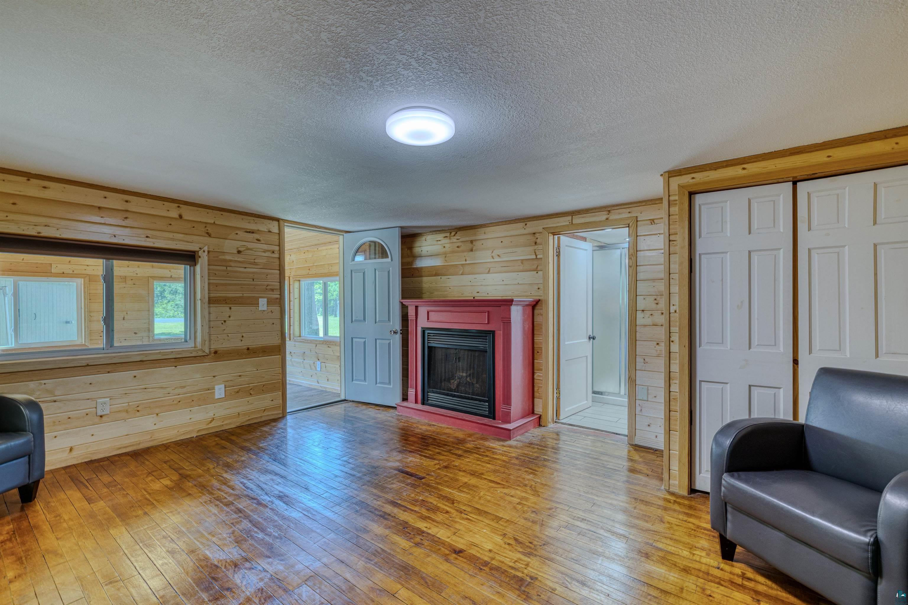 66075 Rooster Road Iron River, WI 54847 - Photo 13 of 52 Living area featuring wood-finish flooring, wood panel walls, and a red-painted fireplace