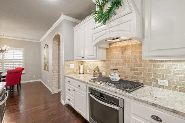 a kitchen with granite countertop a stove a sink dishwasher and white cabinets with wooden floor