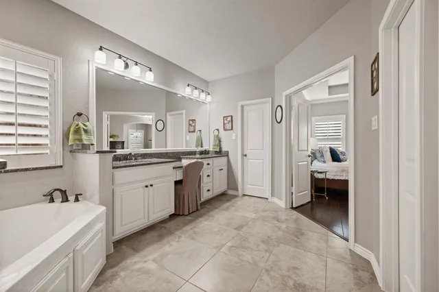 a spacious en suite bathroom with a granite countertop tub double vanity and a mirror