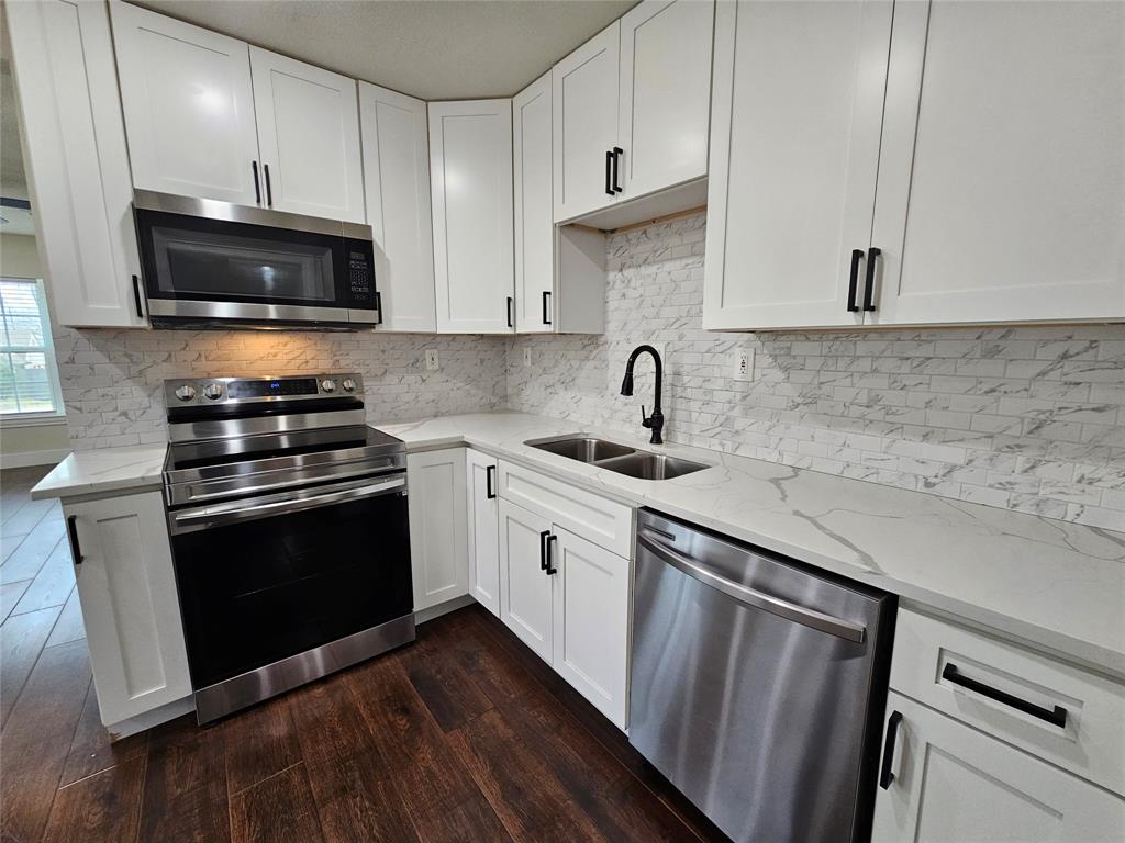 211 North Hampton Road Dallas, TX 75208 - Photo 12 of 22 Modern kitchen featuring white shaker cabinetry, stainless steel appliances, a double basin sink with a matte black faucet, light countertops with prominent veining, and wood-finish flooring
