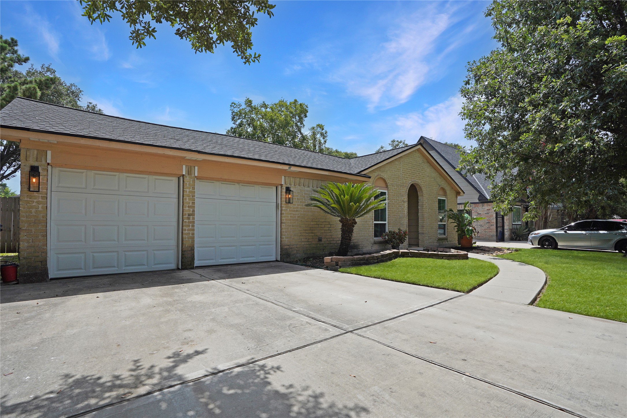 17119 Mellow Ridge Drive Spring, TX 77379 - Photo 2 of 32 This photo showcases a charming single-story brick home with a two-car garage. The front yard is well-maintained, featuring a curved walkway, lush grass, and mature trees, creating a welcoming entrance.