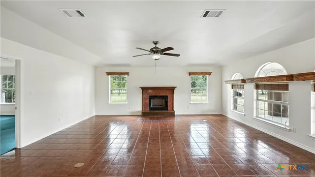 a view of a livingroom with a fireplace a ceiling fan and windows