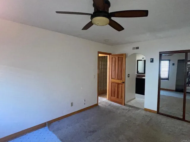 an empty room with chandelier fan and kitchen view