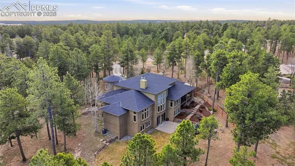 an aerial view of a house around side of green forest