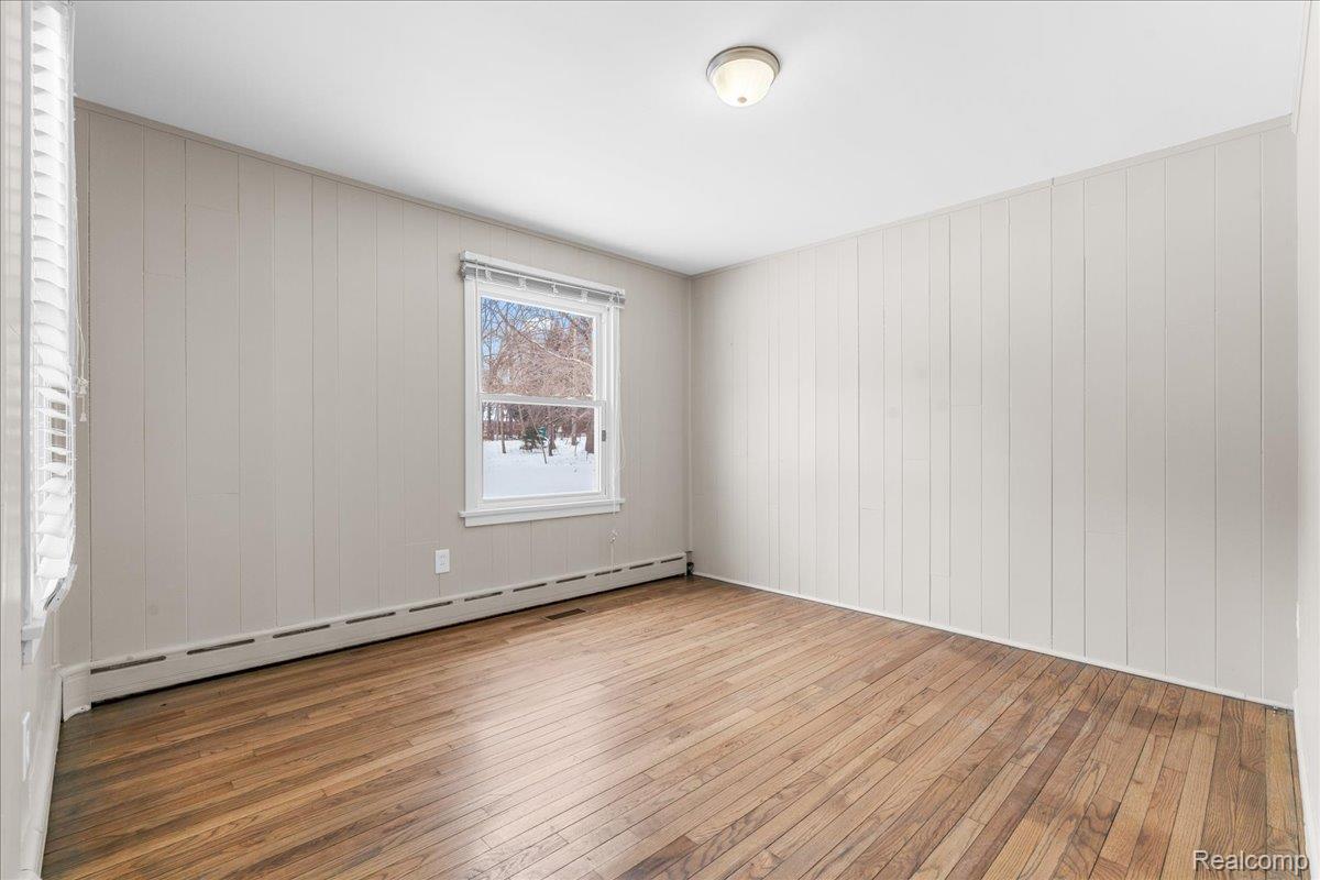 4666 Brighton Road Brighton, MI 48116 - Photo 18 of 37 Spare room featuring wooden walls, hardwood / wood-style floors, and a baseboard heating unit