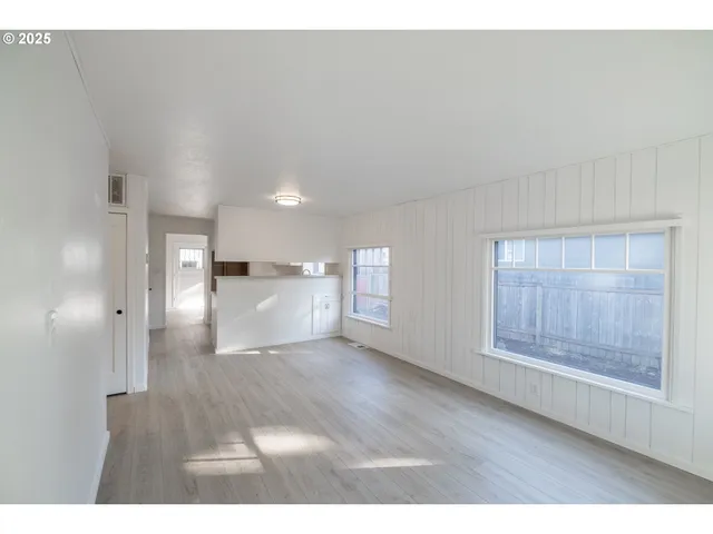 a view of an empty room and a kitchen with wooden floor