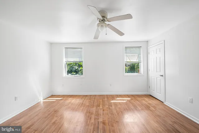 an empty room with wooden floor ceiling fan and windows
