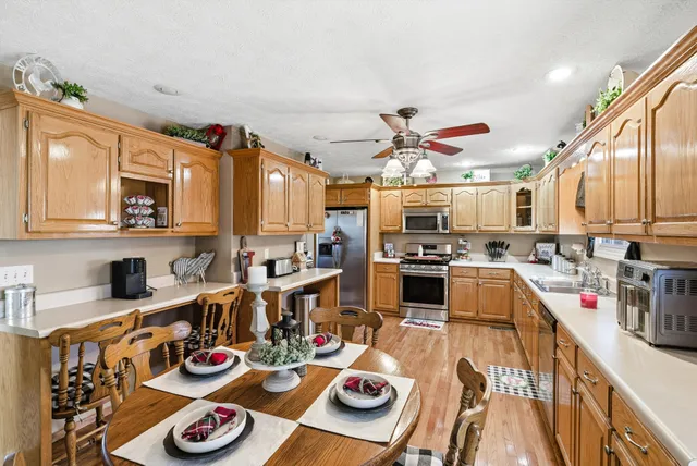 a kitchen with stainless steel appliances granite countertop a stove top oven a refrigerator a dining table and chairs with wooden floor