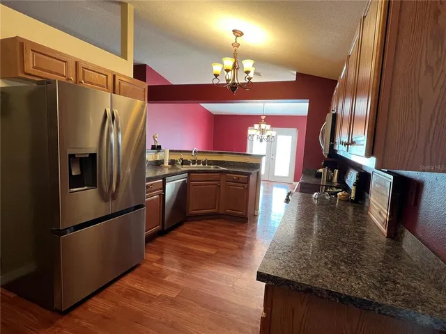 a kitchen with granite countertop a refrigerator a stove and a sink with wooden floor