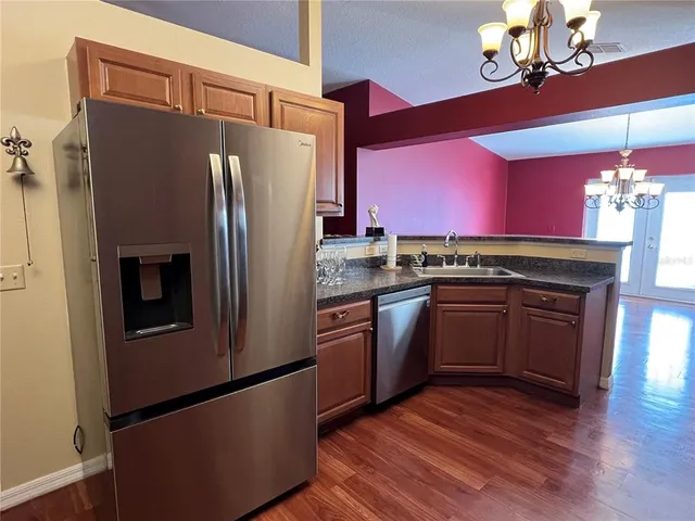 a kitchen with stainless steel appliances granite countertop a refrigerator a sink dishwasher a stove and a dining table with wooden floor