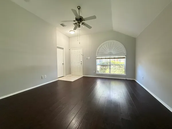 an empty room with wooden floor chandelier fan and windows