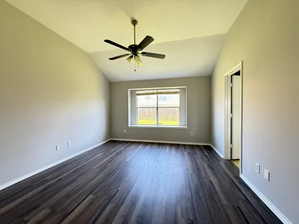 an empty room with wooden floor fan and windows