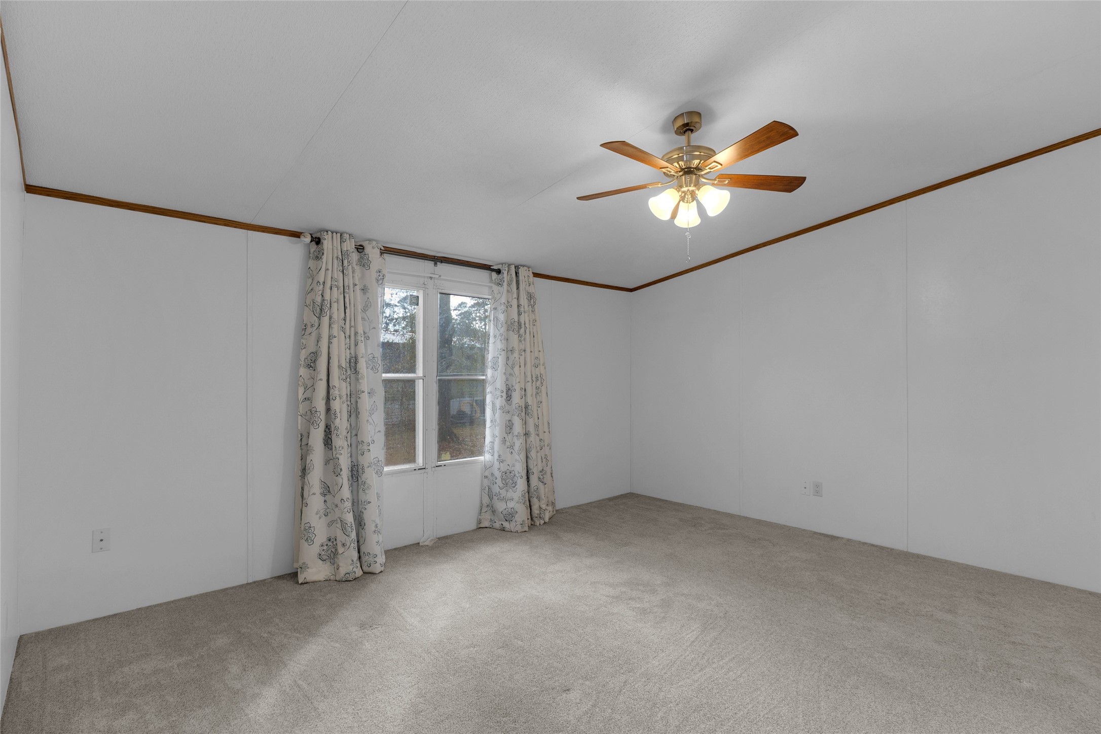 22094 Spear Road Porter, TX 77365 - Photo 31 of 45 Den room offers a generous carpeted space with white walls and a ceiling fan. Sunlight streams through the large window with patterned curtains, enhancing the airy and welcoming atmosphere.