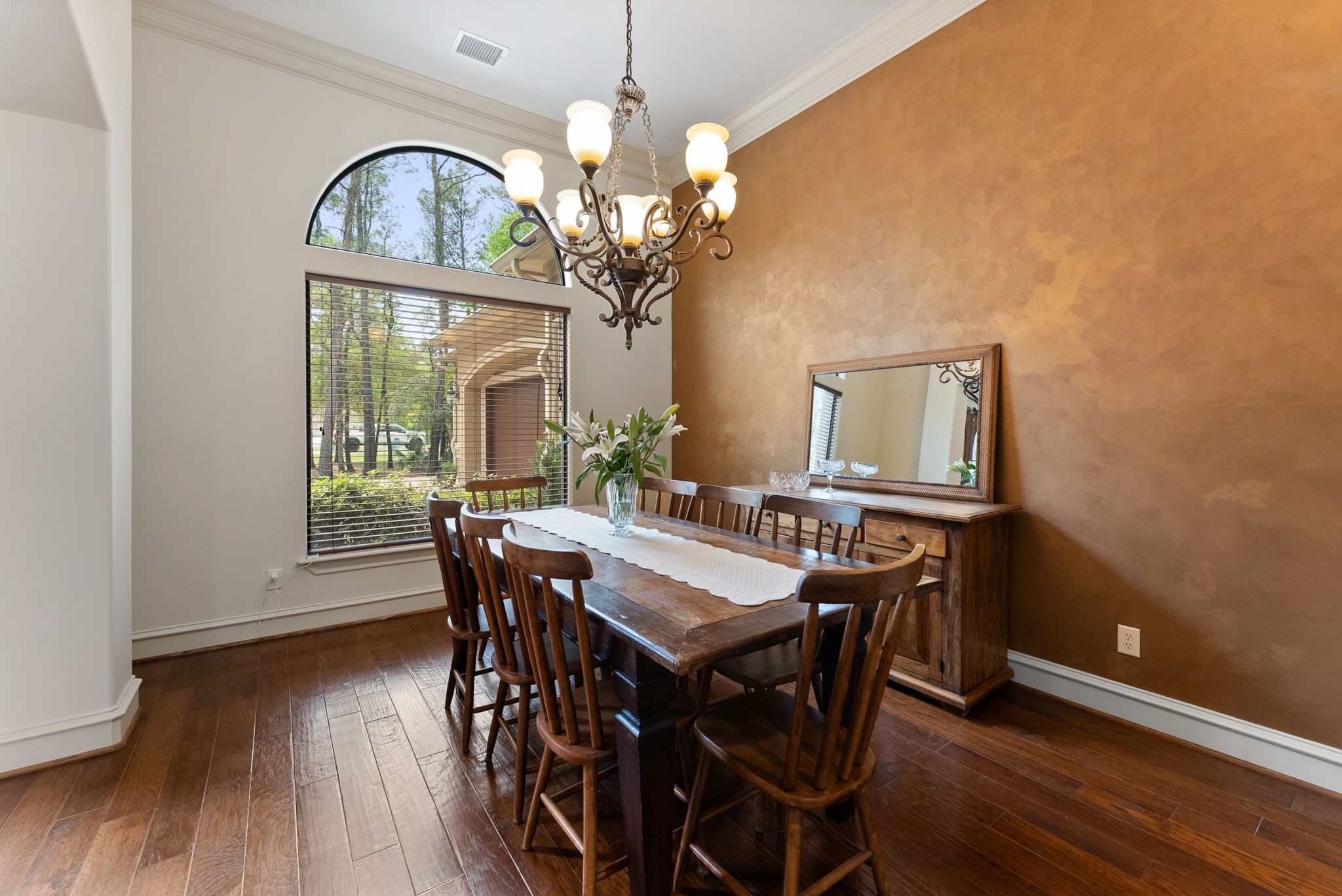 3907 Rayford Road Spring, TX 77386 - Photo 10 of 38 Located just off the foyer, the Formal Dining room features an oversized window with upper transom, arched openings, wood floors, high ceilings, double crown molding, a decorator accent wall, and a hanging light fixture—creating a warm, inviting space for gatherings.