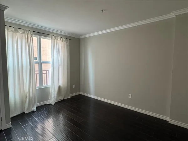 an empty room with wooden floor and windows with curtains