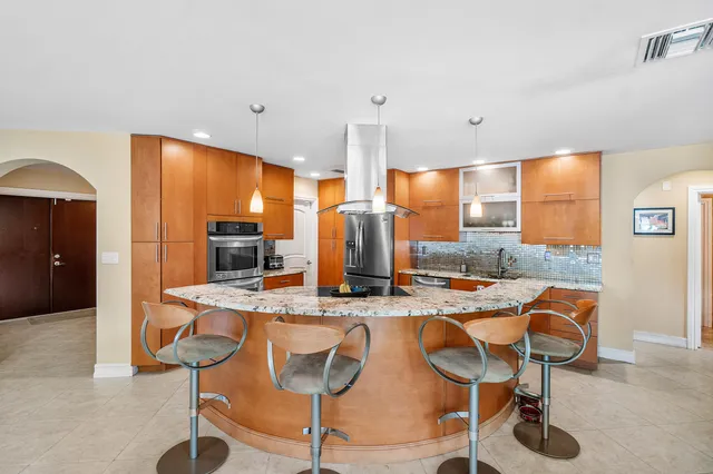 a kitchen with stainless steel appliances kitchen island granite countertop a table chairs and a refrigerator