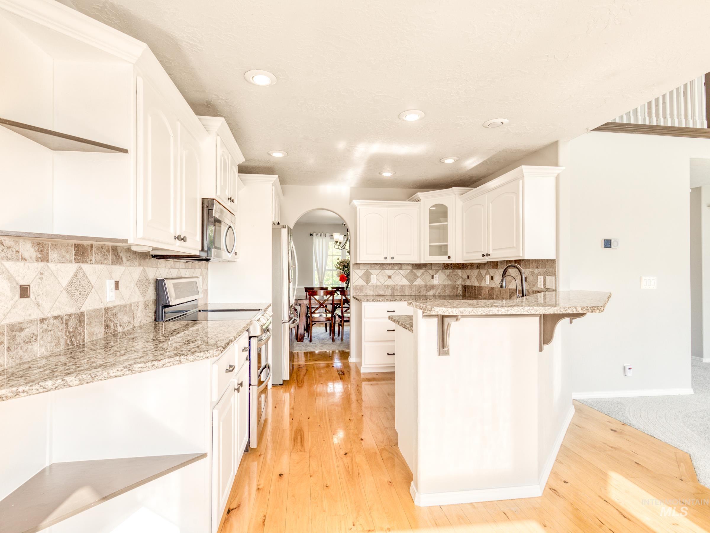 16277 Sand Hollow Road Caldwell, ID 83607 - Photo 16 of 39 Kitchen featuring arched walkways, stainless steel appliances, a kitchen breakfast bar, white cabinetry, and a peninsula