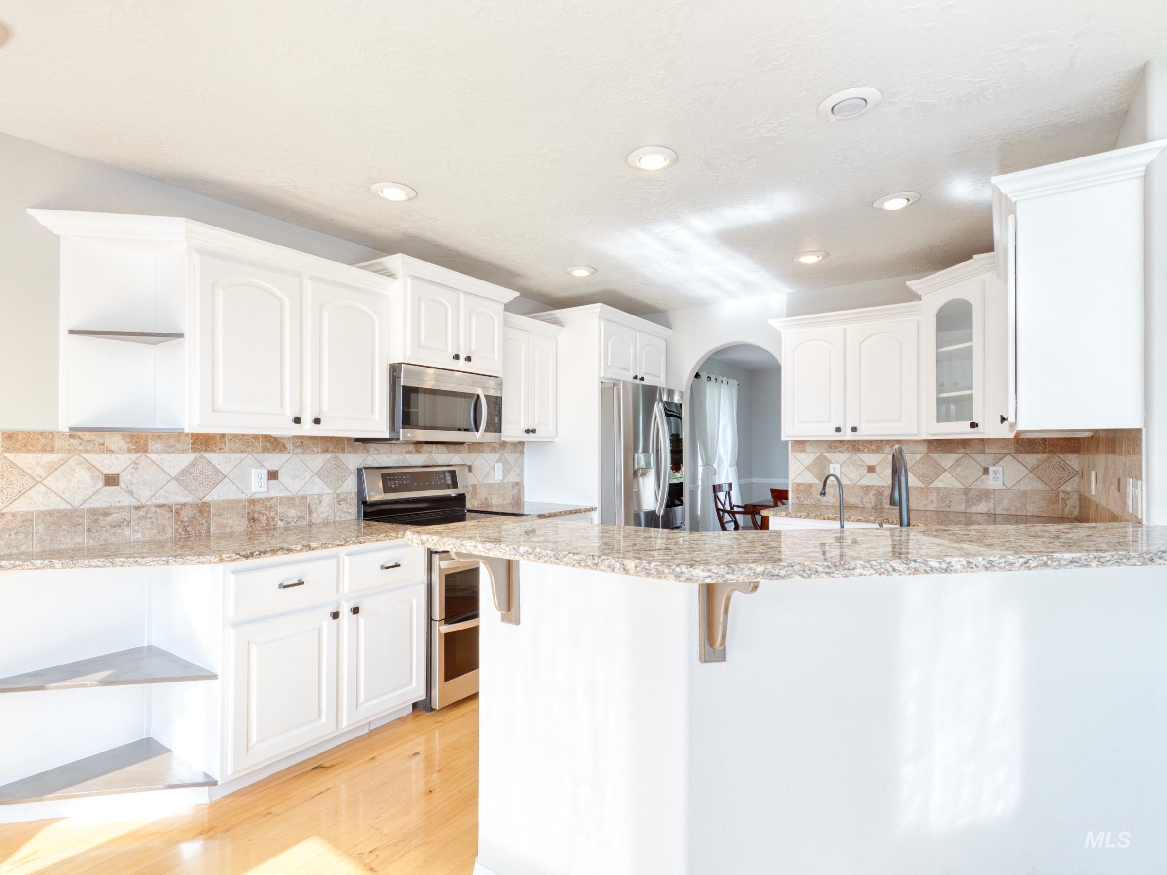 16277 Sand Hollow Road Caldwell, ID 83607 - Photo 17 of 39 Kitchen featuring arched walkways, appliances with stainless steel finishes, a breakfast bar area, white cabinets, and glass insert cabinets