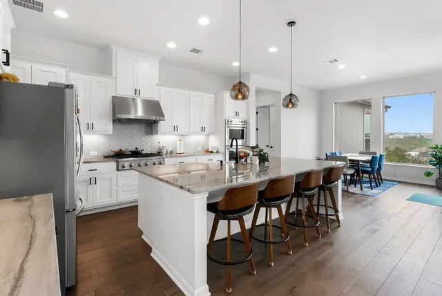 a kitchen with stainless steel appliances a dining table chairs stove refrigerator and cabinets