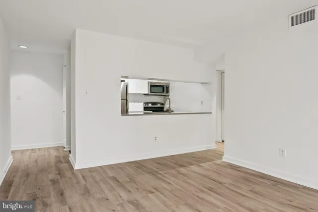 a view of a refrigerator in kitchen and an empty room with wooden floor