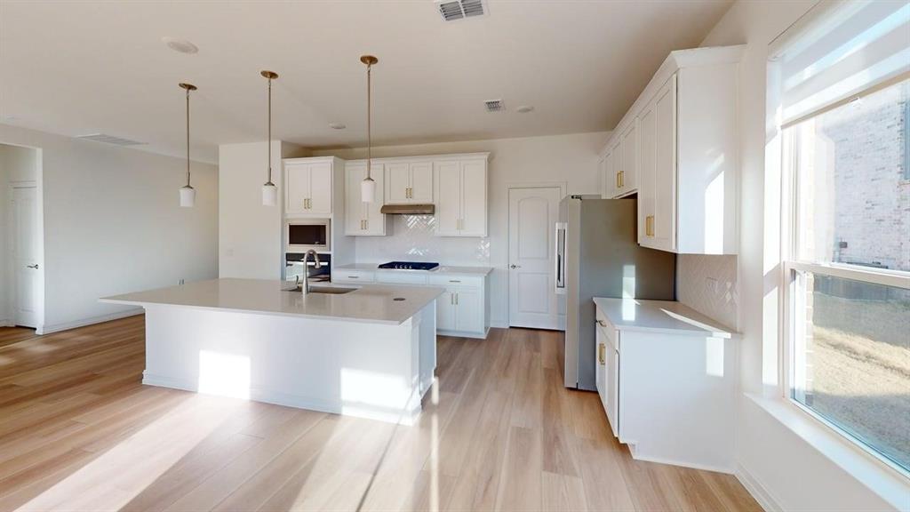 1616 Prosper Lane Anna, TX 75409 - Photo 2 of 24 Kitchen with white cabinetry, a center island with sink, stainless steel appliances, light wood finished floors, and pendant lighting