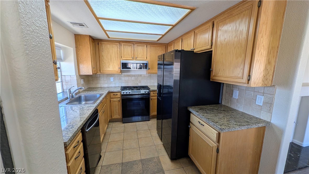 1685 Strasbourg Way, Unit 1685 Henderson, NV 89014 - Photo 11 of 22 Kitchen featuring a textured wall, black appliances, backsplash, and wood finish cabinetry