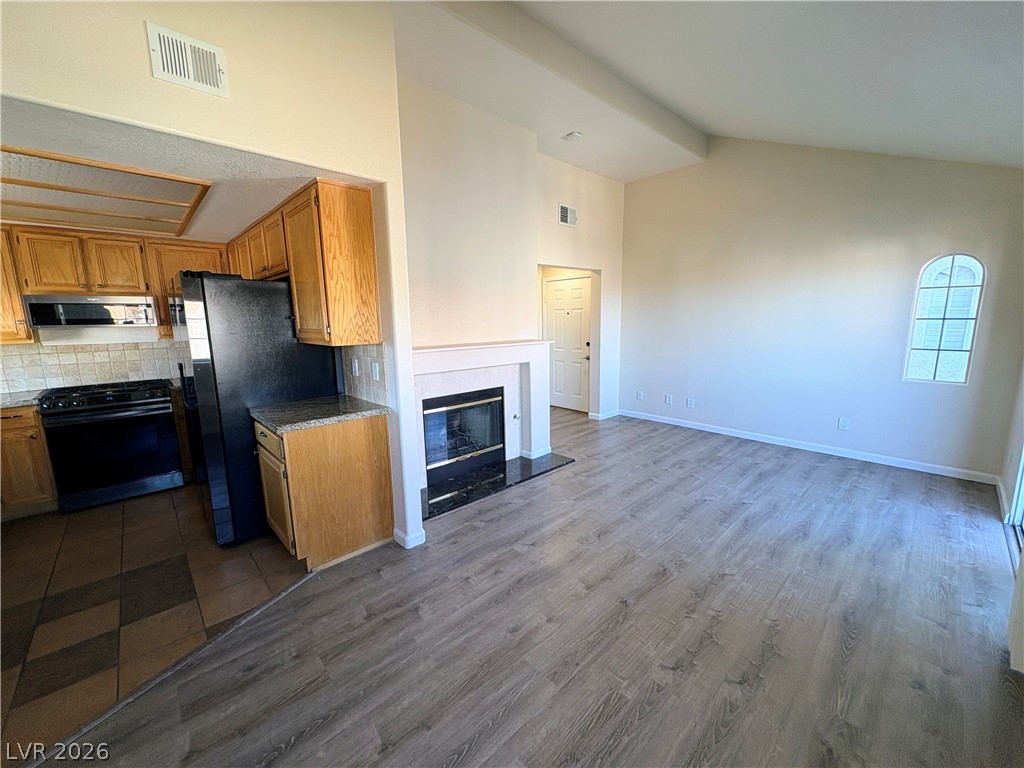 1685 Strasbourg Way, Unit 1685 Henderson, NV 89014 - Photo 4 of 22 Kitchen featuring wood finish cabinets, black appliances, decorative backsplash, dark wood-style floors, and vaulted ceiling