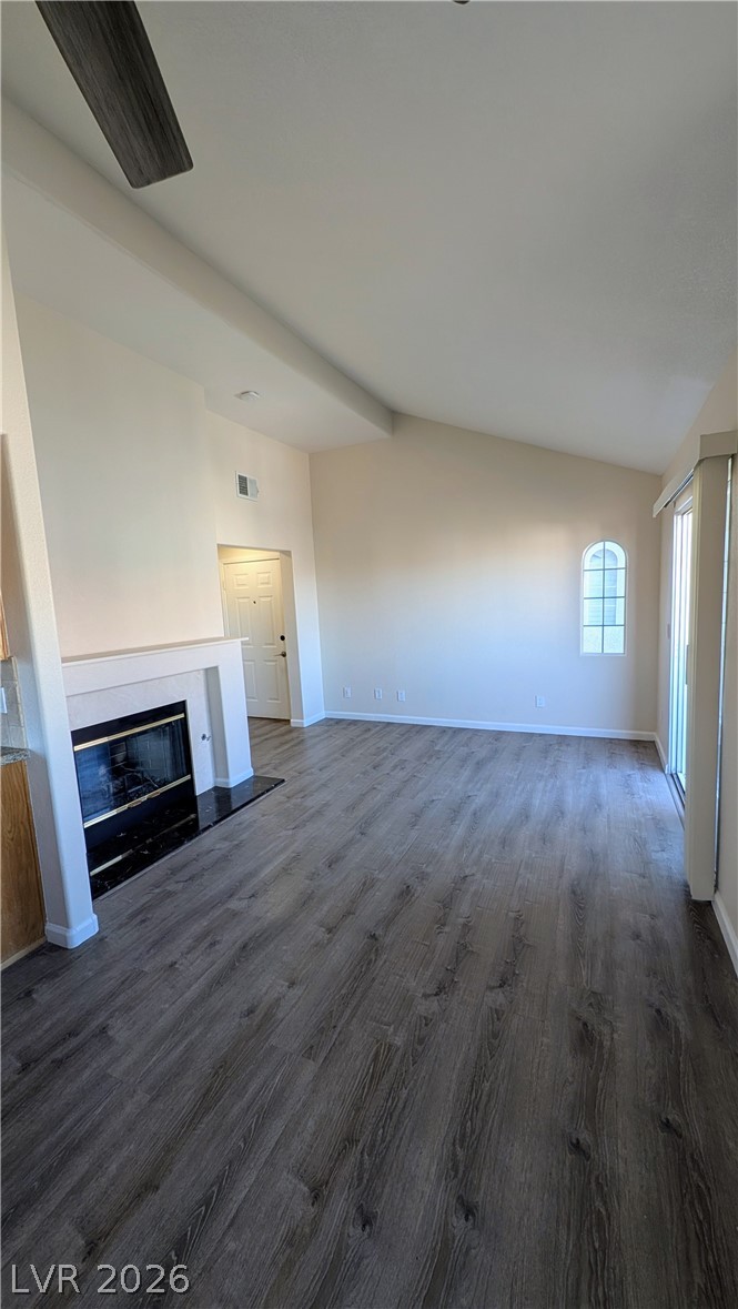 1685 Strasbourg Way, Unit 1685 Henderson, NV 89014 - Photo 6 of 22 Unfurnished living room featuring vaulted ceiling with beams, a glass covered fireplace, dark wood-type flooring, and a ceiling fan